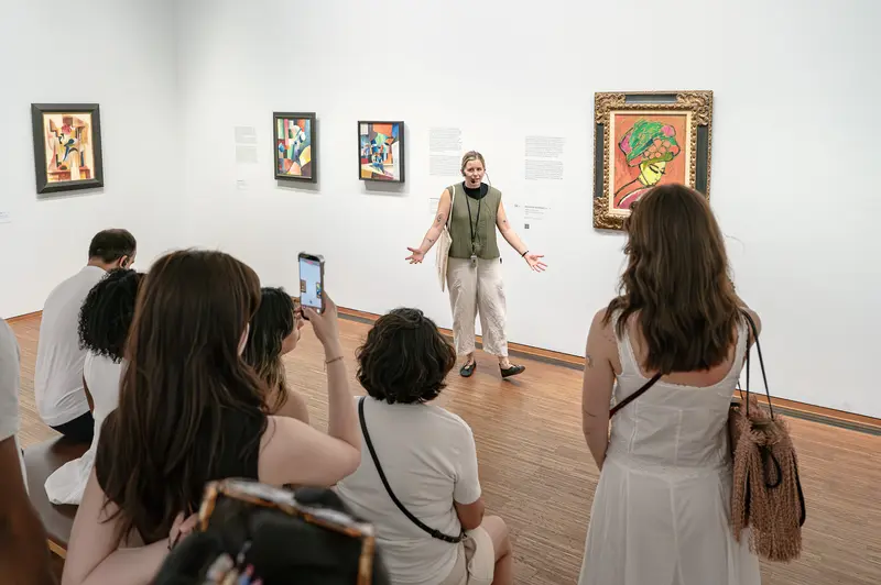 Museum Docent Leading Gallery Tour Among Framed Artworks
