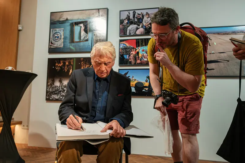 Don McCullin Signs Book While Attendee Photographs at Leica Gallery Vienna