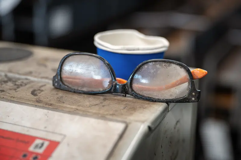 Dust-coated safety glasses and paper cup on a steel workbench at Frankstahl