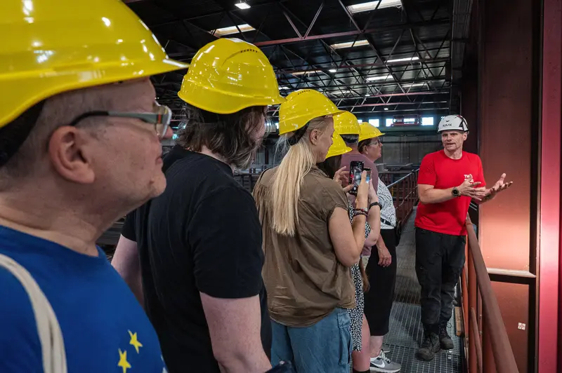 Tour group in yellow hard hats receives briefing inside Frankstahl warehouse