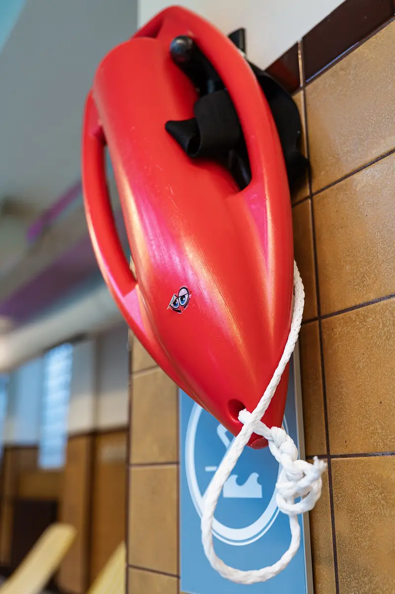 Red rescue buoy mounted on brown-tiled wall at Amalienbad
