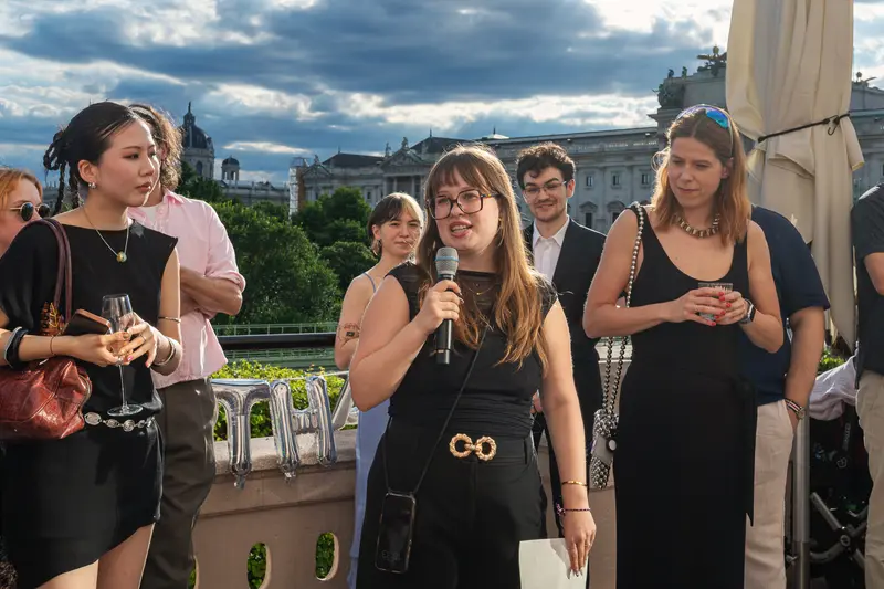 Speaker Addresses Guests at Rooftop Event with Vienna Kunsthistorisches Museum Backdrop
