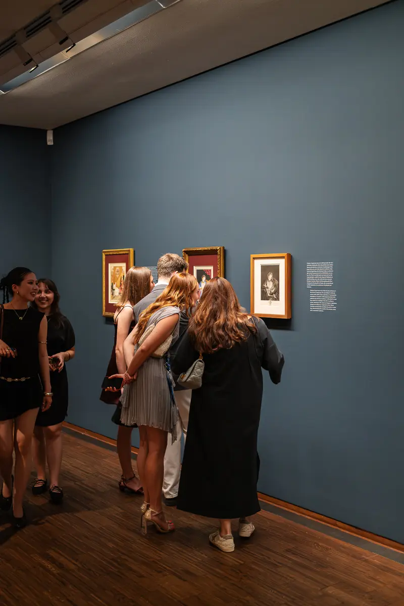 Visitors Examining Framed Artworks on Blue Gallery Wall