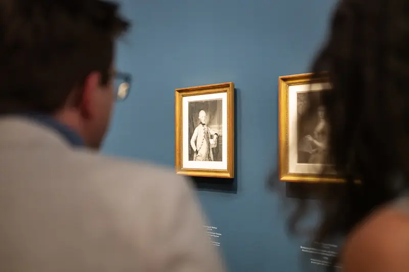 Visitors Viewing Framed Portrait Engravings on Blue Gallery Wall