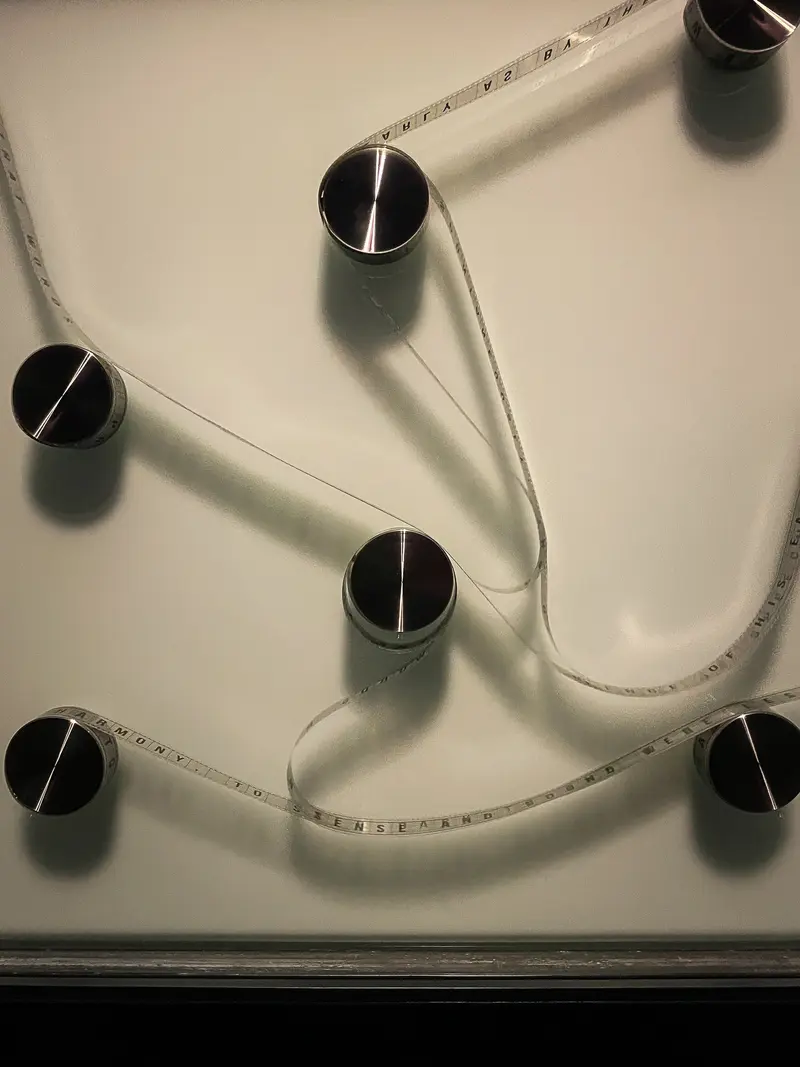 Measuring Tape Weaving Between Cylindrical Objects on White Surface