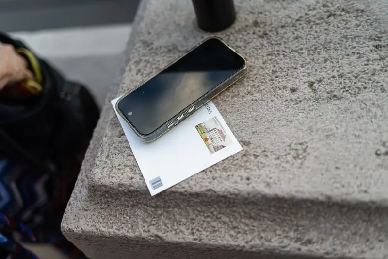 Smartphone and Postcard Resting on Stone Ledge Outdoors