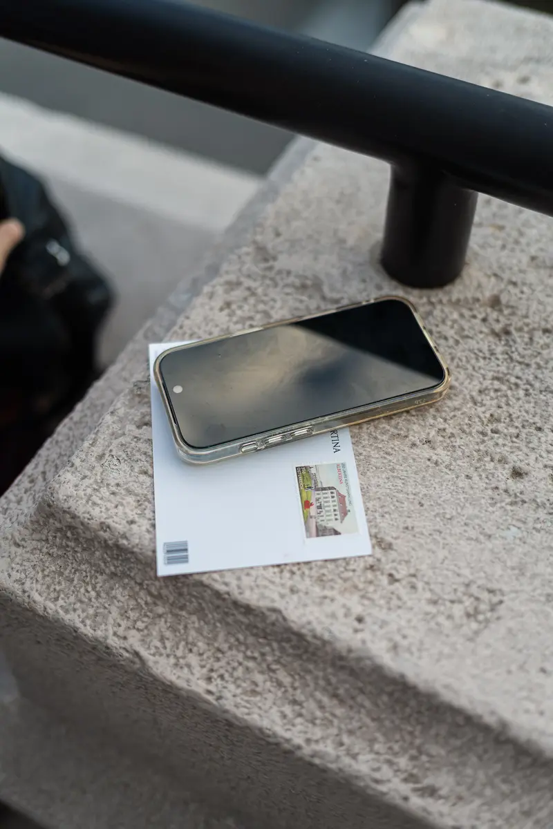 Smartphone and Illustrated Postcard Resting on Concrete Ledge