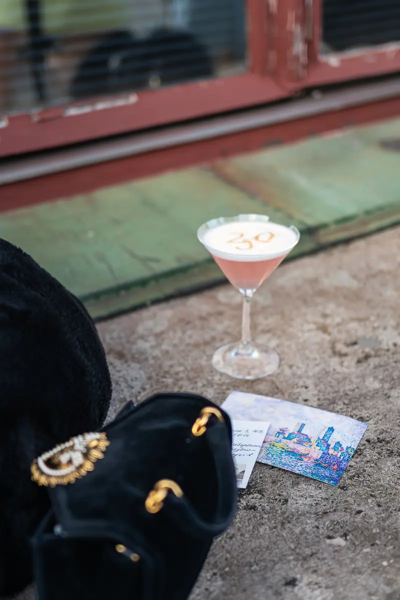 Cocktail with "30" Foam Art and Event Ticket Beside Velvet Bag