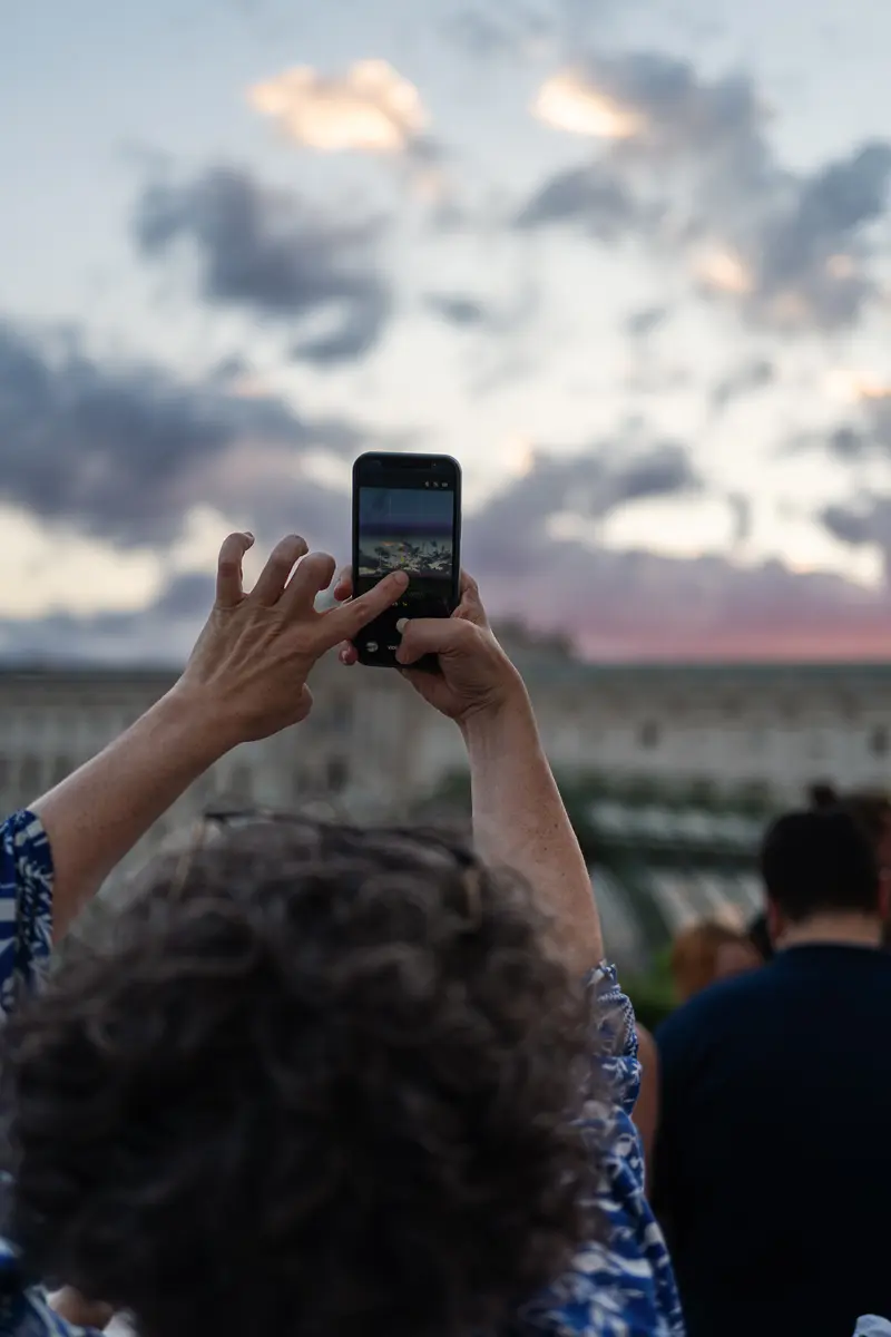 Attendee Photographing Sunset Sky on Smartphone at Outdoor Event