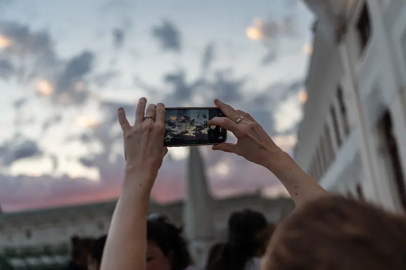 Attendee Photographing Sunset Sky with Smartphone at Outdoor Event