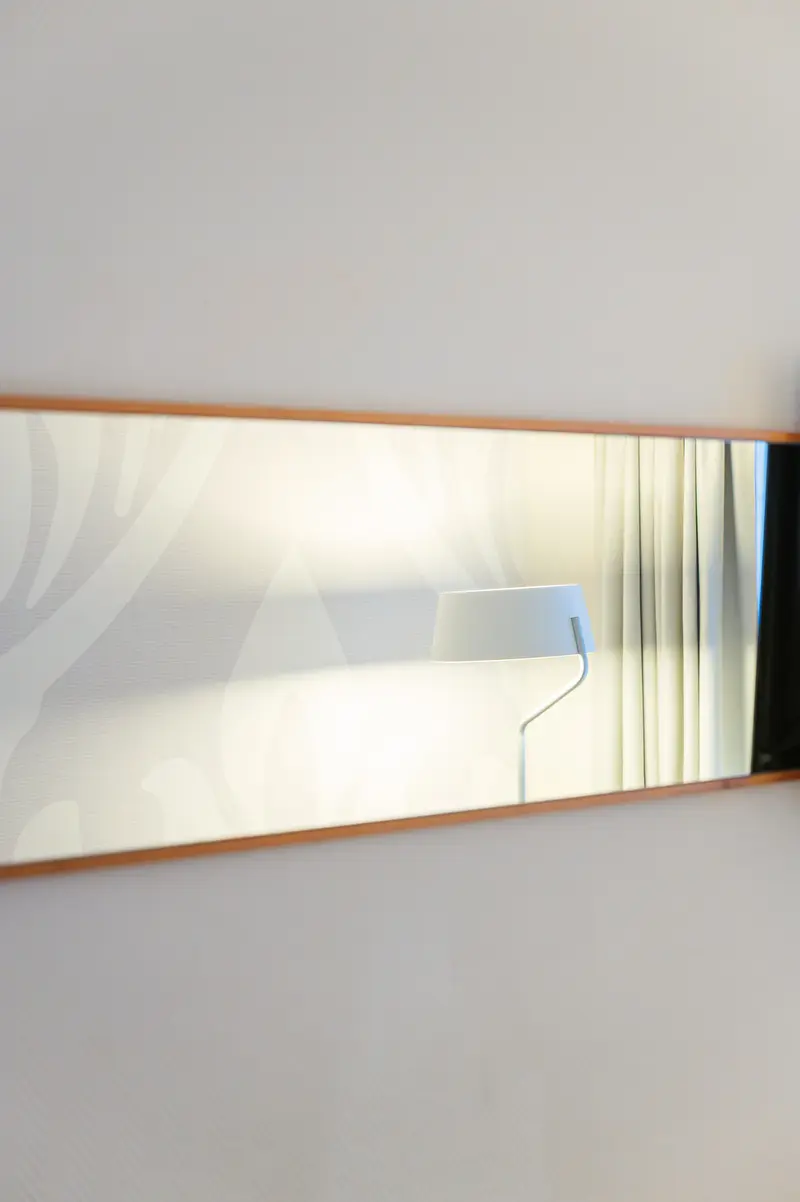 Wood-framed mirror reflecting lamp in guest room at Hotel Das Tigra, Vienna