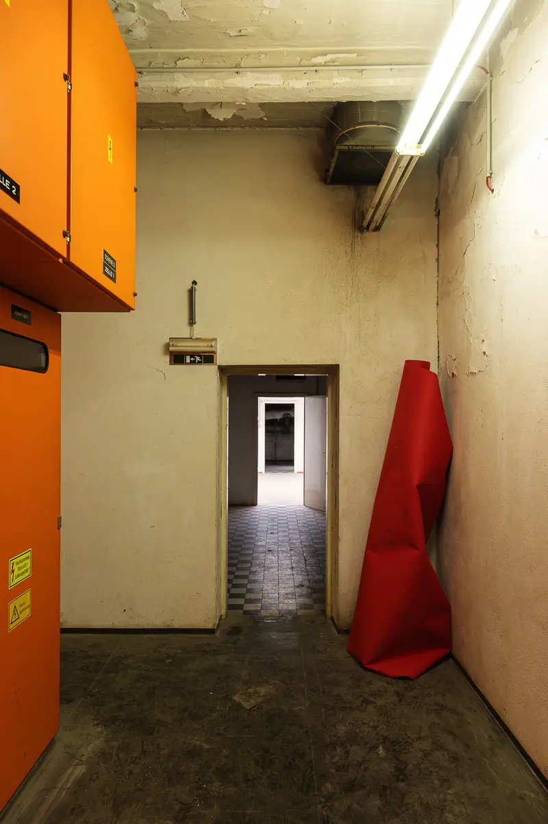 Orange electrical cabinets and rolled red carpet in Glanzstoff St. Pölten interior corridor