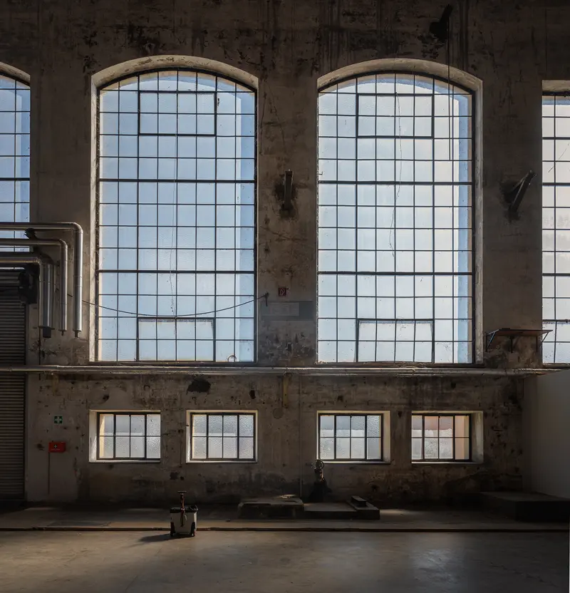 Arched steel-framed factory windows in empty Glanzstoff production hall, St. Pölten