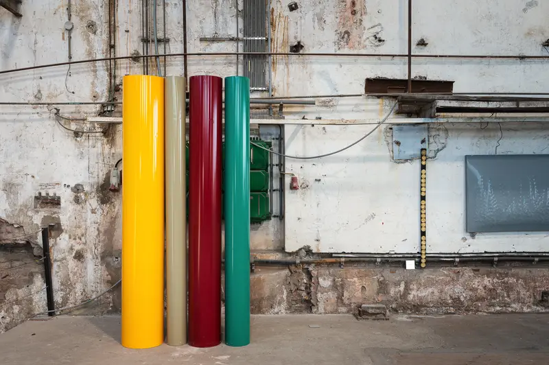 Four coloured steel columns against weathered factory wall, Glanzstoff St. Pölten Open House 2026