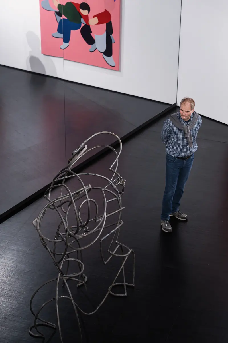 Visitor viewing a bent-steel figure sculpture at Marko Sajn "Becoming One" opening, Strabag Art Site