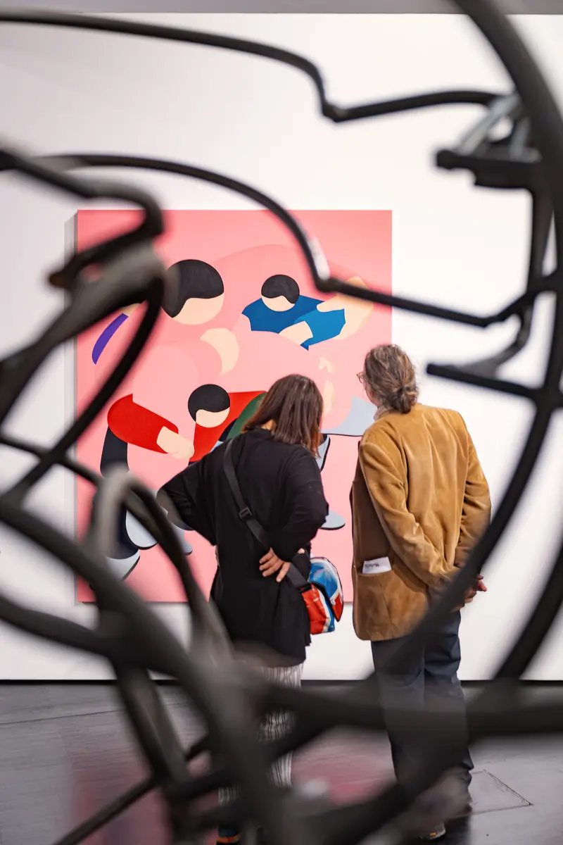 Two visitors viewing a pink Marko Sajn painting through a black wire sculpture at Strabag Art Site